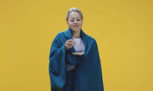 Femme enveloppée dans une couverture, savourant une tasse de tisane chaude pour se réchauffer et soulager les inconforts de l'hiver.