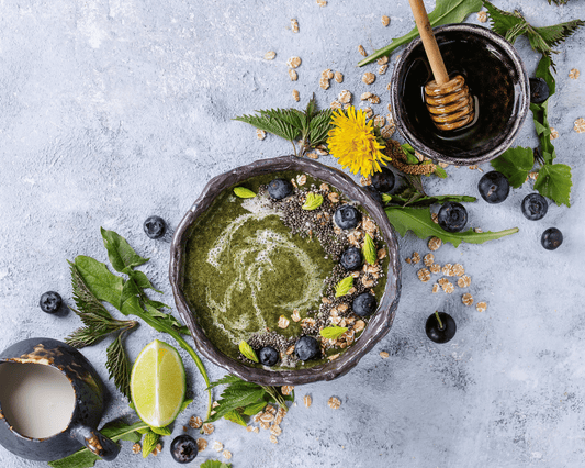 Smoothie détox à l'ortie accompagné de plantes médicinales fraîches, miel et myrtilles, parfait pour une détox printanière naturelle.