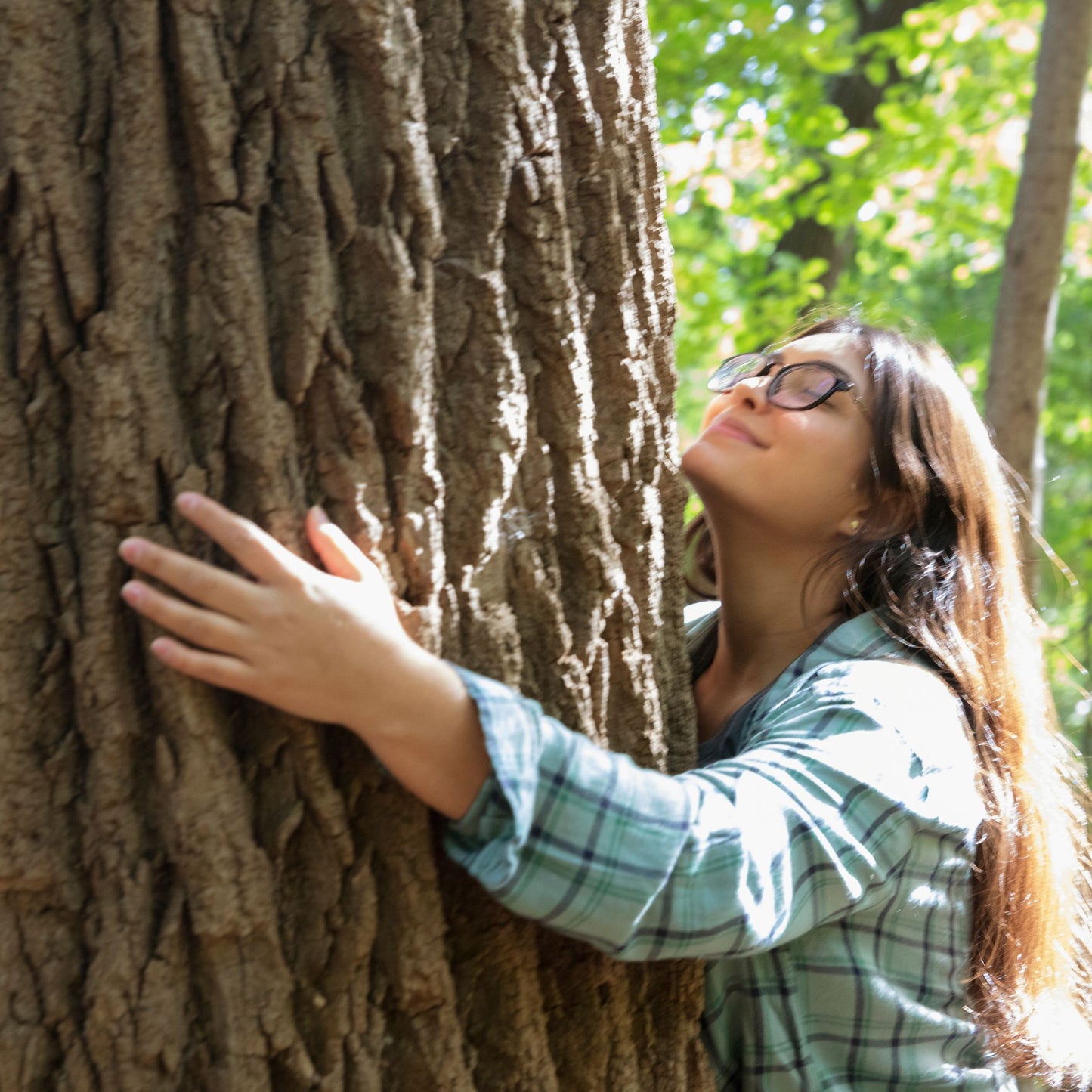Femme aux longs cheveux roux embrassant le tronc d'un grand arbre en forêt, les yeux fermés et le visage tourné vers la lumière, exprimant une connexion profonde avec la nature