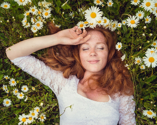 Femme souriante et détendue allongée dans un champ de camomille en fleurs, évoquant la relaxation et le bien-être naturel