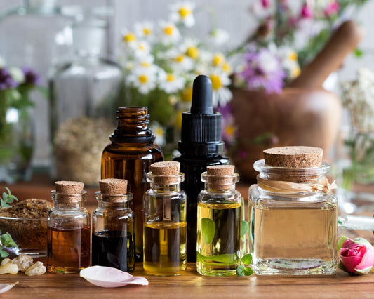 Flacons d’huiles essentielles avec pétales de rose et mortier, entourés de plantes médicinales, pour la fabrication de remèdes naturels contre les douleurs articulaires et musculaires