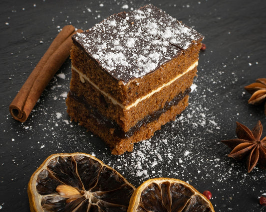 Morceau de pain d’épices posé sur une ardoise noire, saupoudré de sucre glace, accompagné d’une branche de cannelle, d’anis étoilé et de rondelles d’oranges séchées.