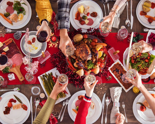Vue d’une table de Noël festive avec plats généreux et mains levant des verres pour un toast, ambiance chaleureuse et conviviale des fêtes.