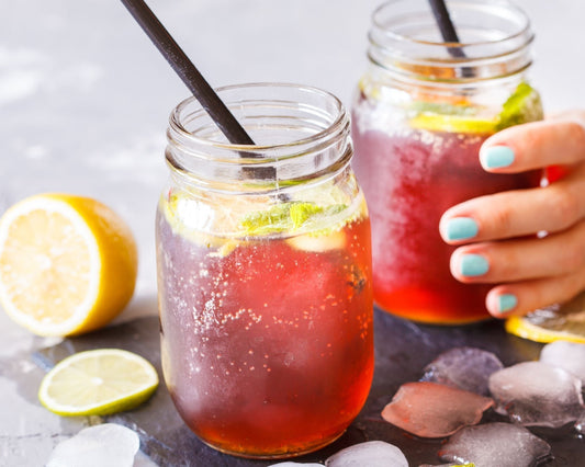 Deux verres de cocktails glacés maison à base de sirops rouges, avec glaçons, citron et une main tenant un verre – boisson rafraîchissante d’été