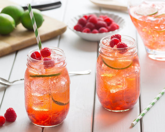 Deux grands verres d’eau fraîche garnis de glaçons, tranches de citron vert et framboises, avec des fruits frais autour