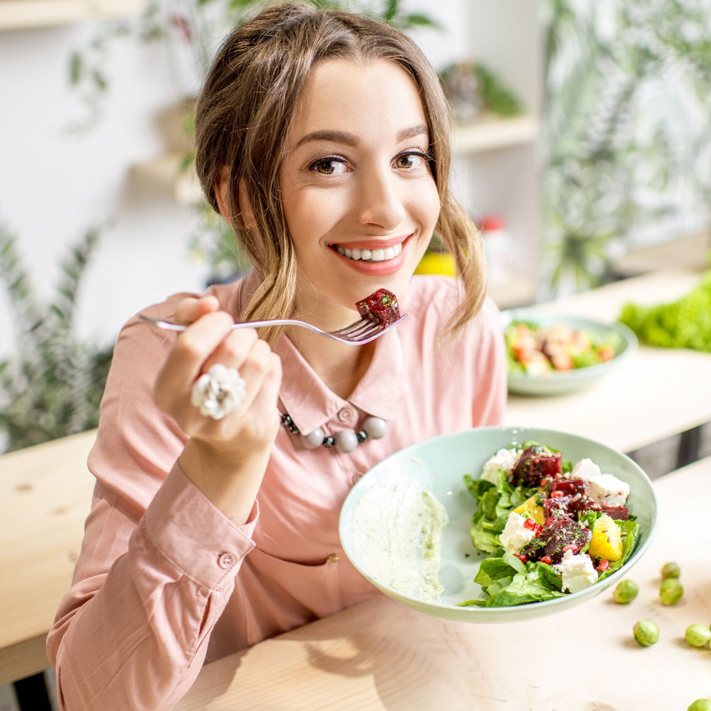 Jeune femme souriante qui mange une salade colorée, illustrant les bienfaits d'une alimentation naturelle et saine