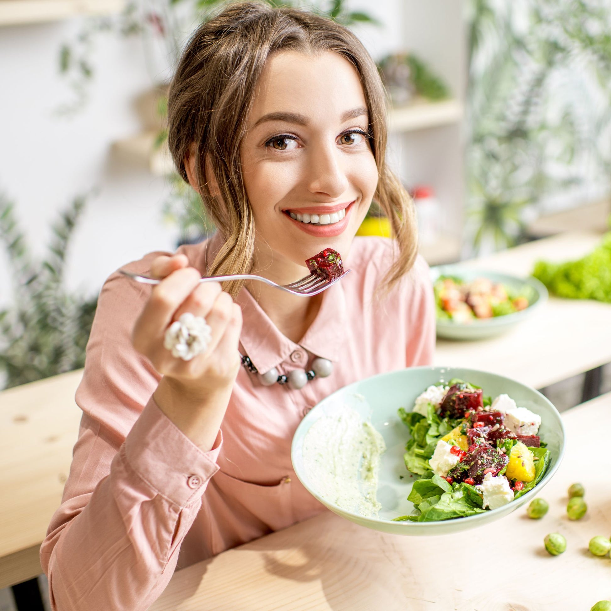 Jeune femme souriante qui mange une salade colorée, illustrant les bienfaits d'une alimentation naturelle et saine