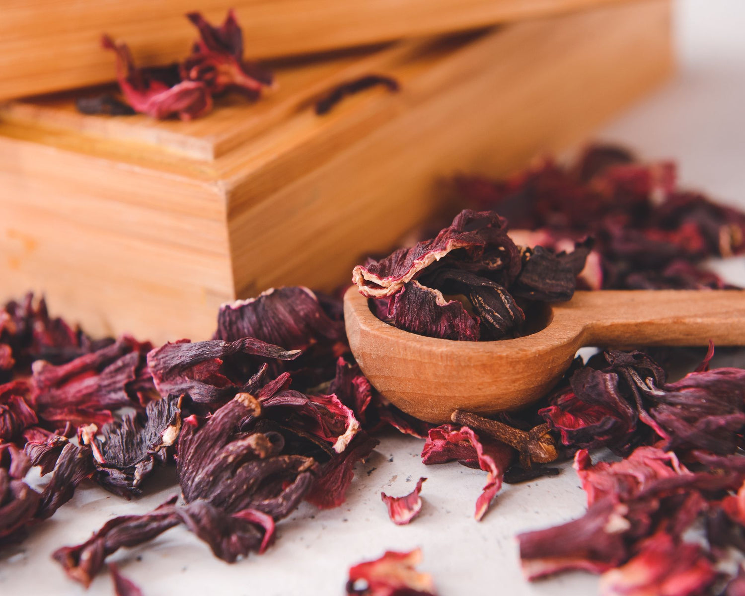 Boîte en bois fermée entourée de fleurs d’hibiscus séchées avec une cuillère en bois remplie de pétales
