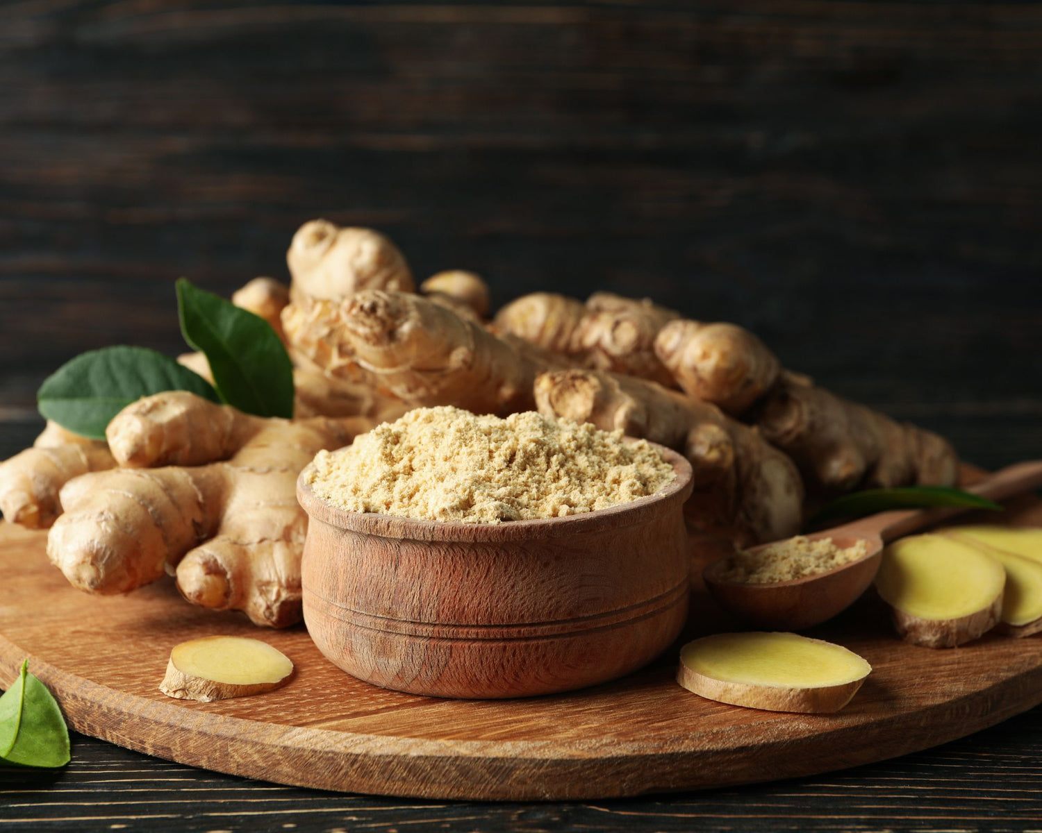 Rhizomes de gingembre frais, rondelles de gingembre et gingembre moulu dans un récipient, présentés sur une planche en bois