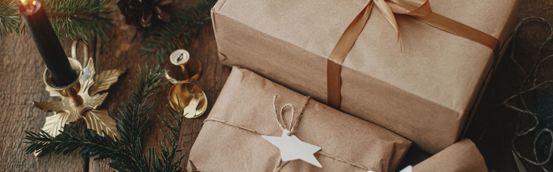 Cadeaux emballés en papier kraft décorés de branches de sapin et d’éléments de Noël, accompagnés d’une bougie chaleureuse. Ambiance festive invitant à offrir des coffrets cadeaux bien-être pour les fêtes.