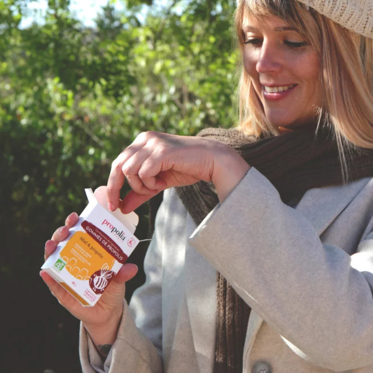  Femme souriante en pleine nature tenant un sachet de Gommes de Propolis® au miel Propolia — le bien-être au quotidien pour toute la famille 
